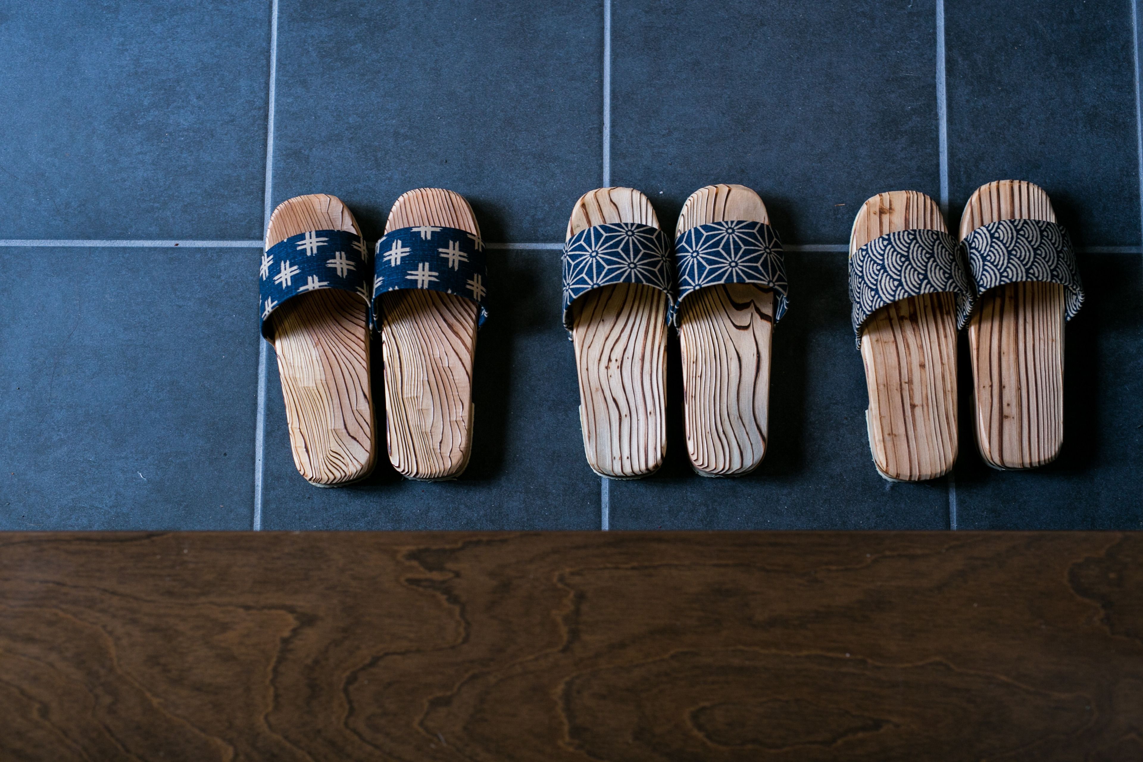 A row of wooden sandals with different patterns on a tiled floor.