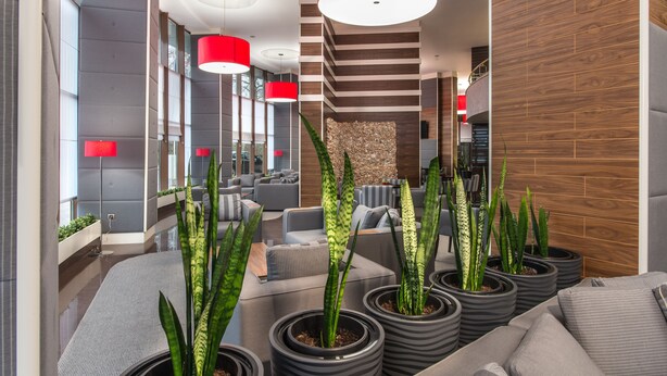 Un hall d’entrée moderne avec des canapés gris, des plantes en pot et des luminaires suspendus rouges.