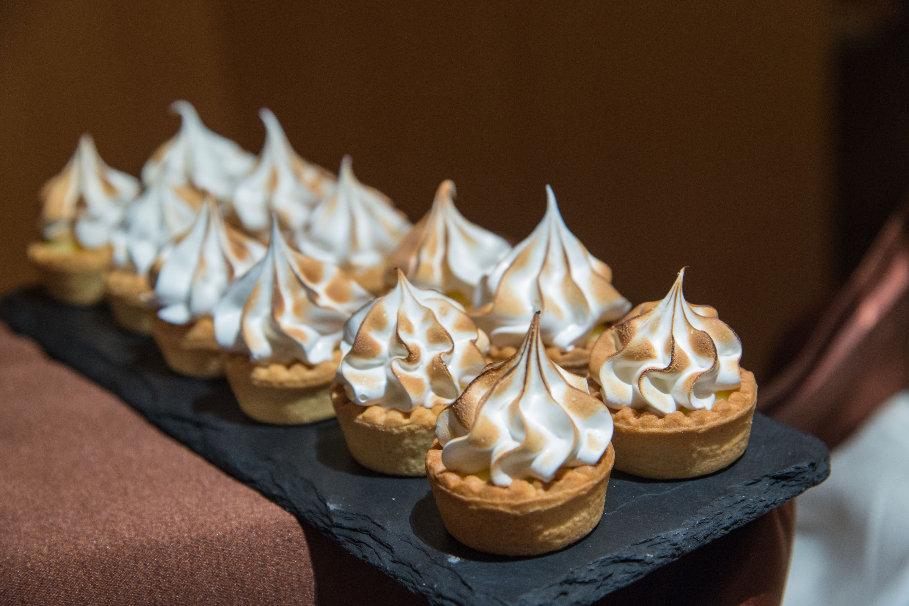 A row of mini tarts with whipped cream on a slate serving board.