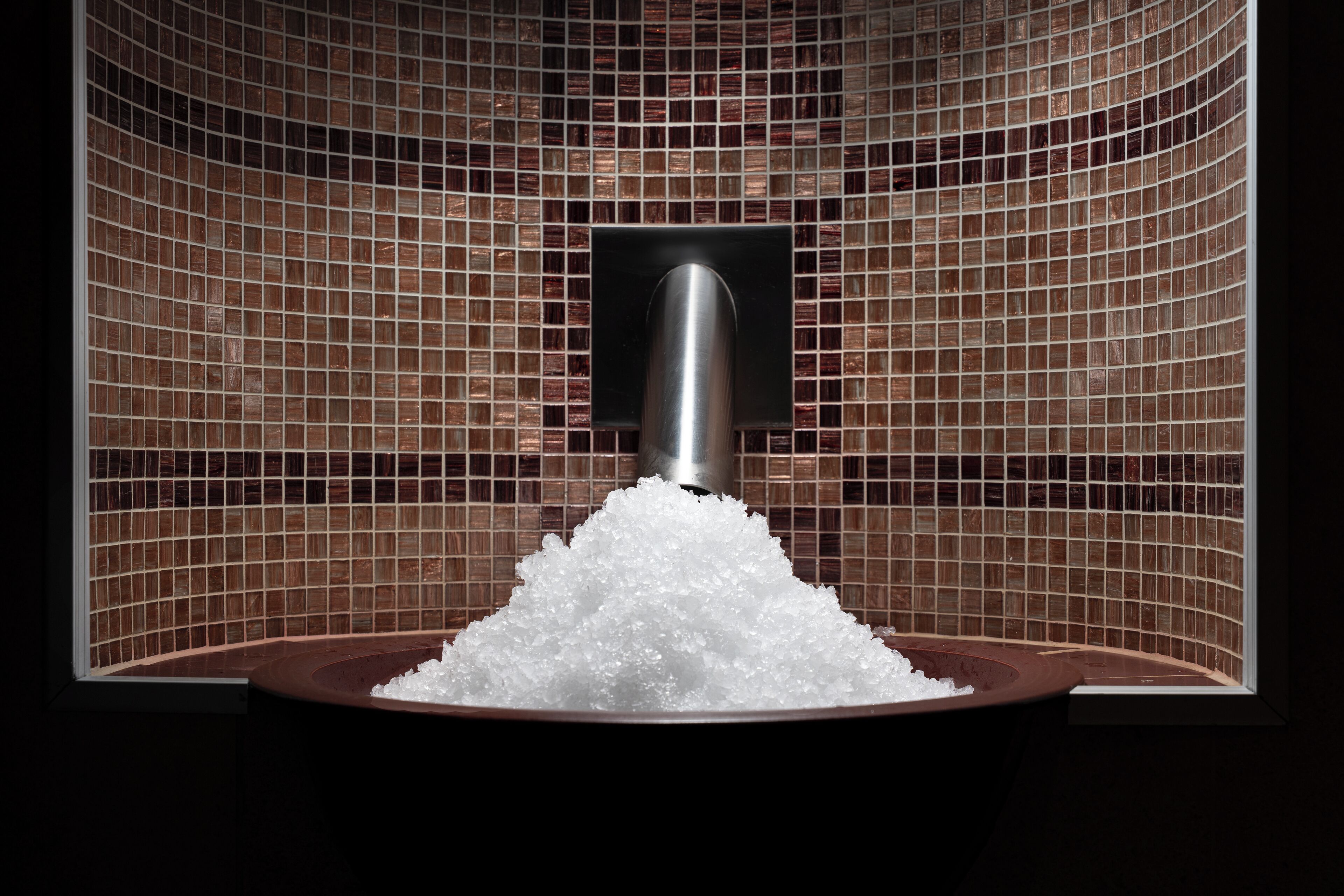 A bathroom with a tiled wall, a sink, and a showerhead.