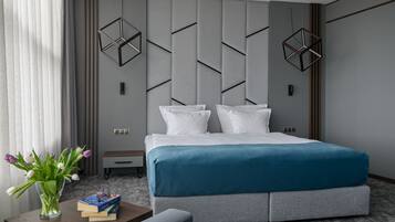 A modern hotel room with a large bed, a bedside table with books and a vase of flowers, and geometric wall panels.