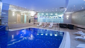 Une piscine intérieure moderne avec une eau d’un bleu cristallin, des chaises longues et un espace d’accueil doté d’un mur en verre.