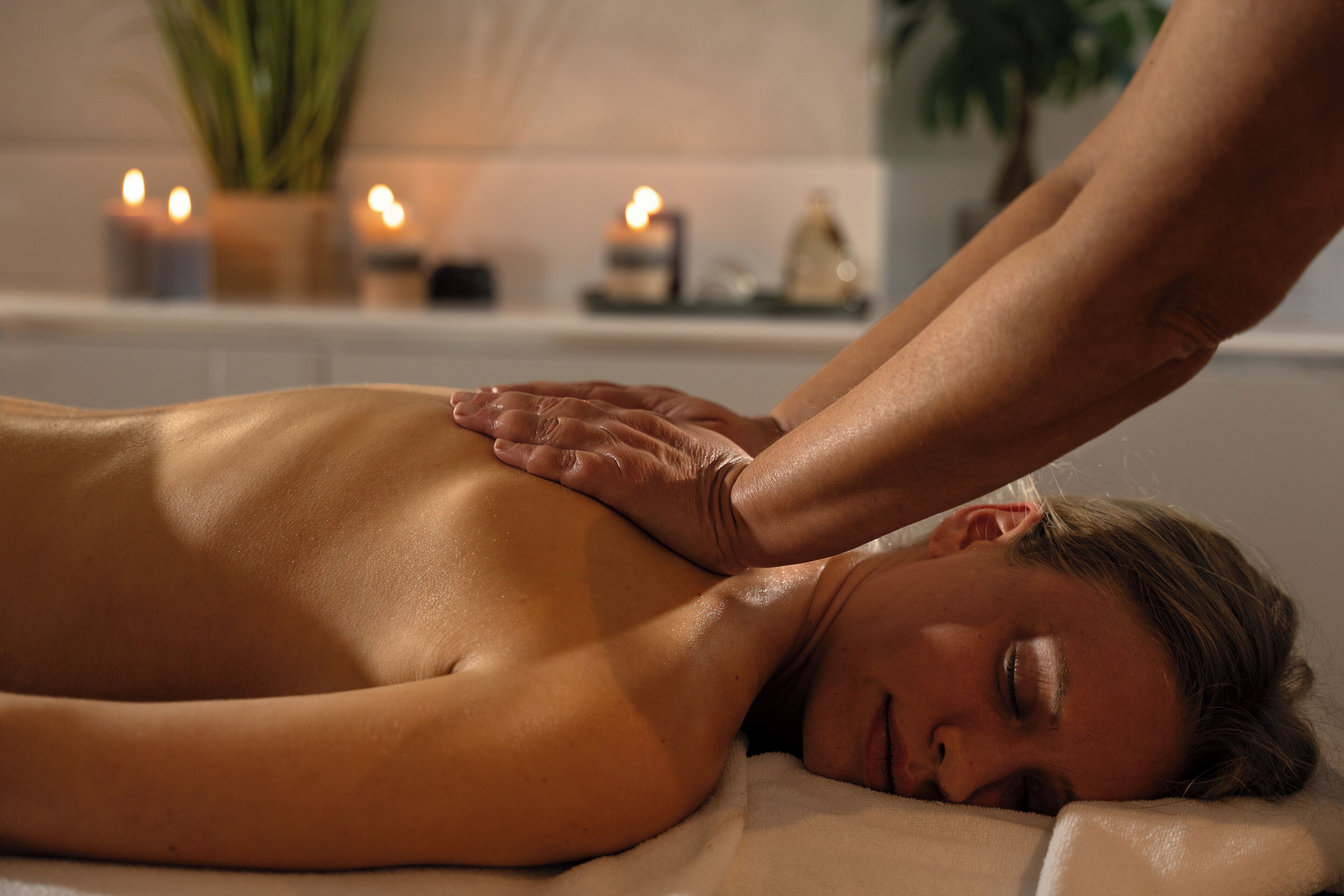 A person receiving a massage in a room with candles and a plant in the background.
