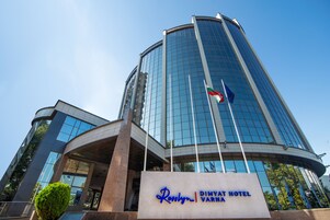 Exterior del hotel Ronlyn Dimyat Varmia, con fachada moderna de vidrio y una entrada destacada con un cartel.