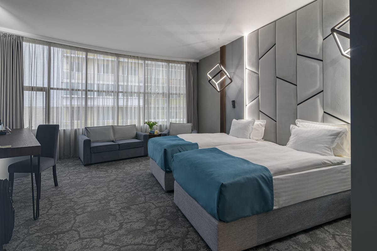 A modern hotel room with a large bed, two bedside tables, a desk, and a sofa.