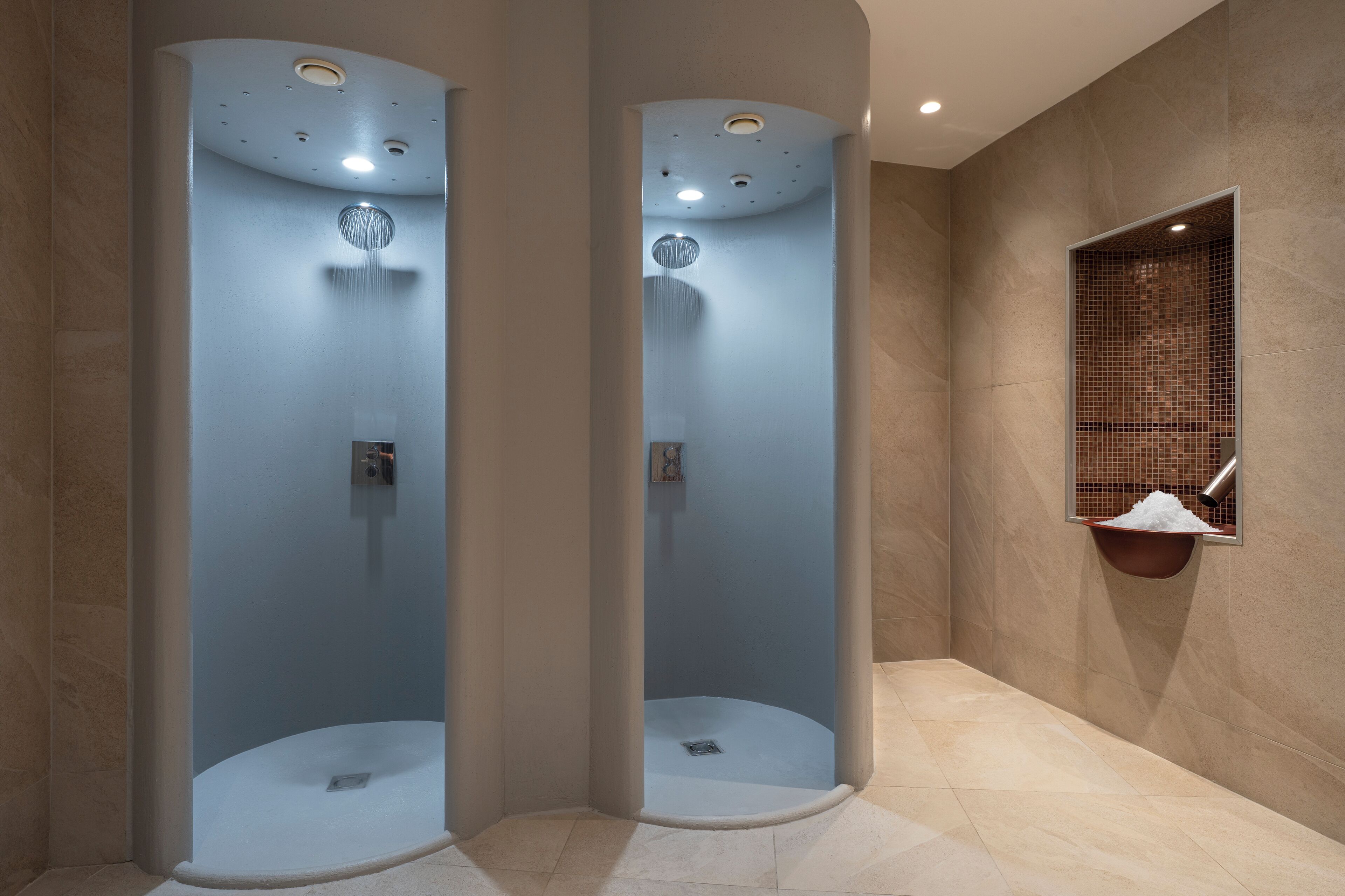 Ein modernes Badezimmer mit zwei raumhohen Glasduschen, Fliesenboden und einem kleinen Waschbecken mit gefliestem Becken.