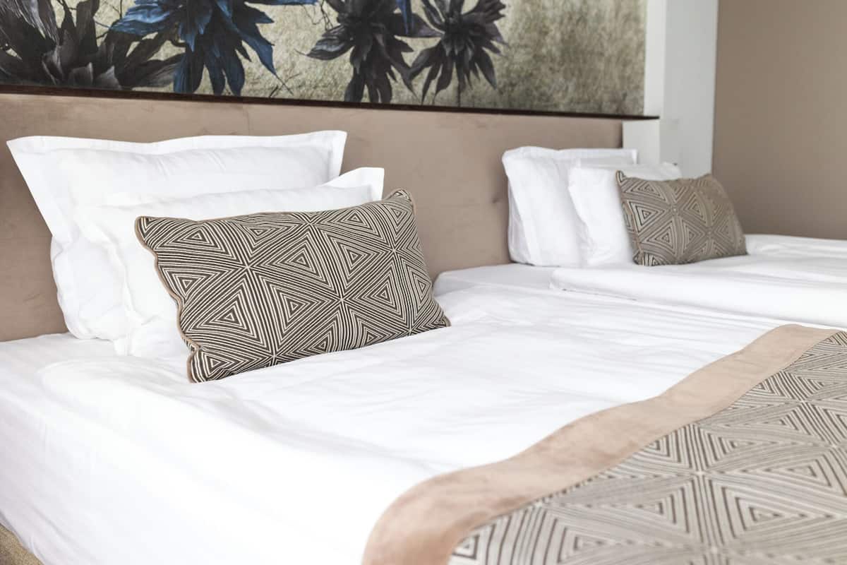 A hotel room with two beds, each with white bedding and patterned pillows.