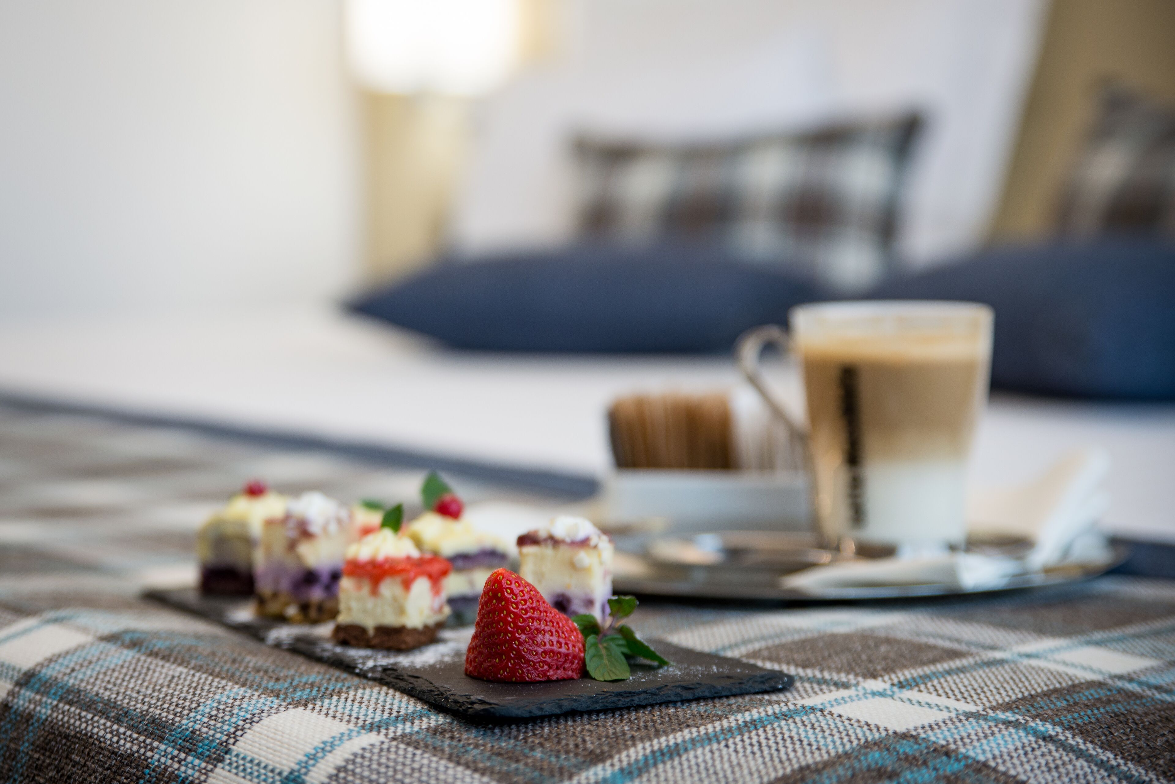 A dining table with a plaid tablecloth, a cup of coffee, and a plate of desserts.