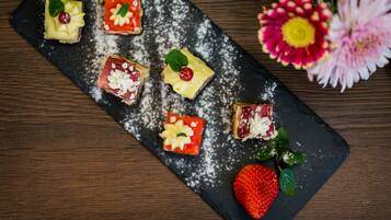 A slate serving board with six square desserts, each topped with a cherry and mint leaves, and a whole strawberry with leaves.
