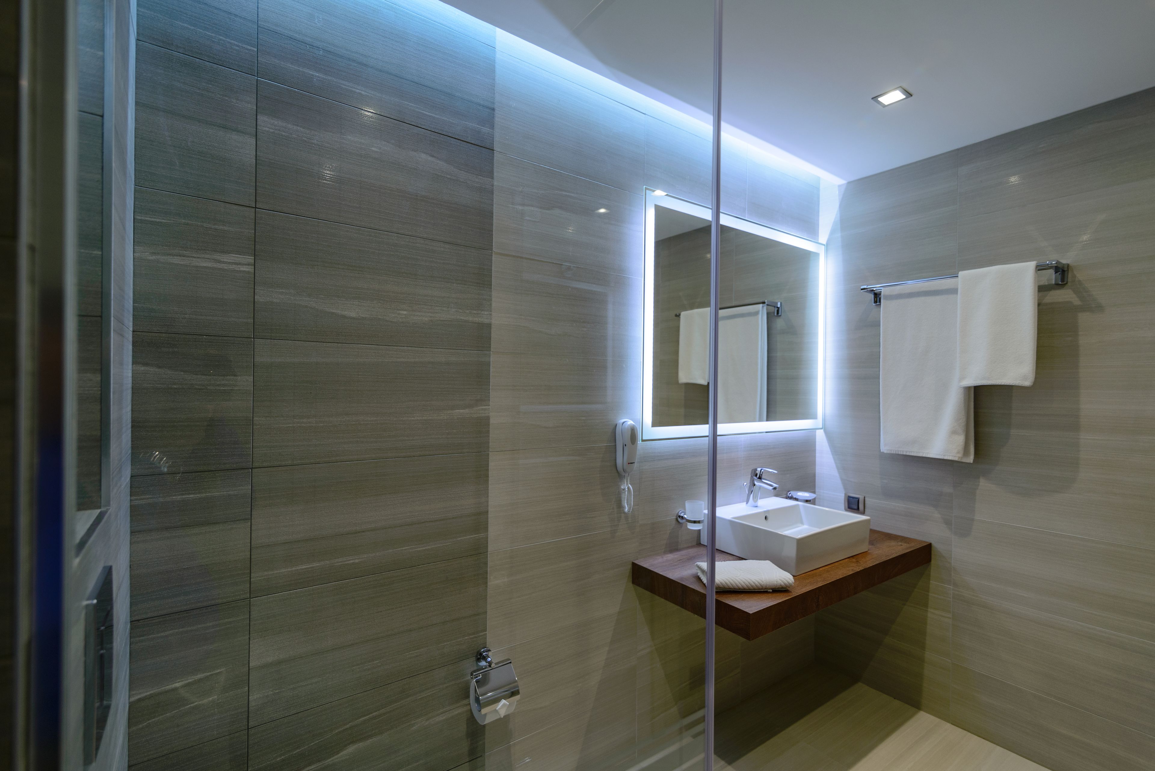 A modern bathroom with a glass shower enclosure, a wooden vanity, a white sink, and a mirror.
