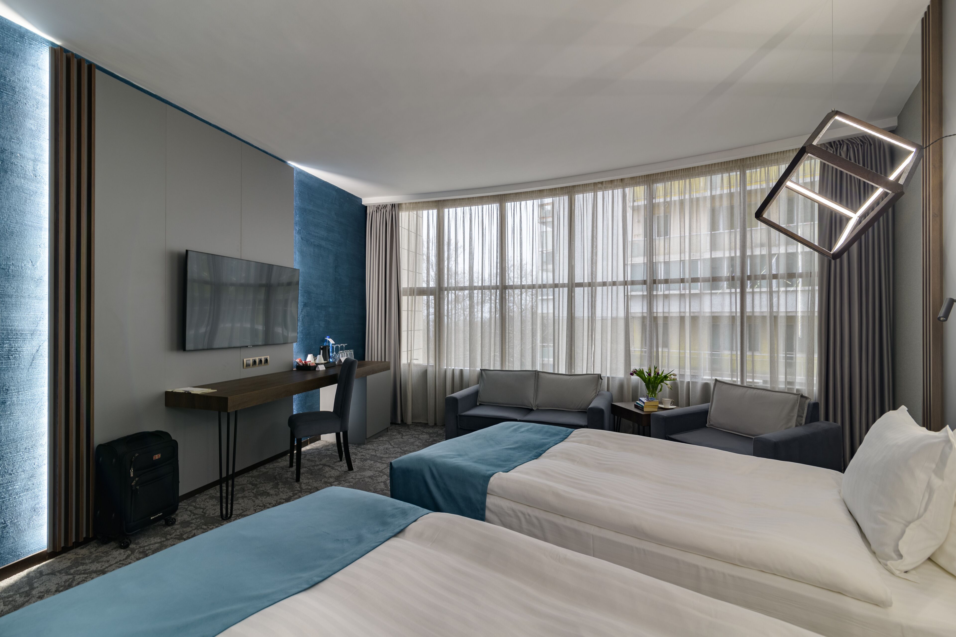 Een hotelkamer met twee bedden, een bureau, een televisie en een groot raam met gordijnen.