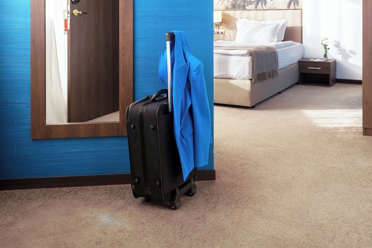 A hotel room with a large mirror, a suitcase, and a bed with a floral wall mural.