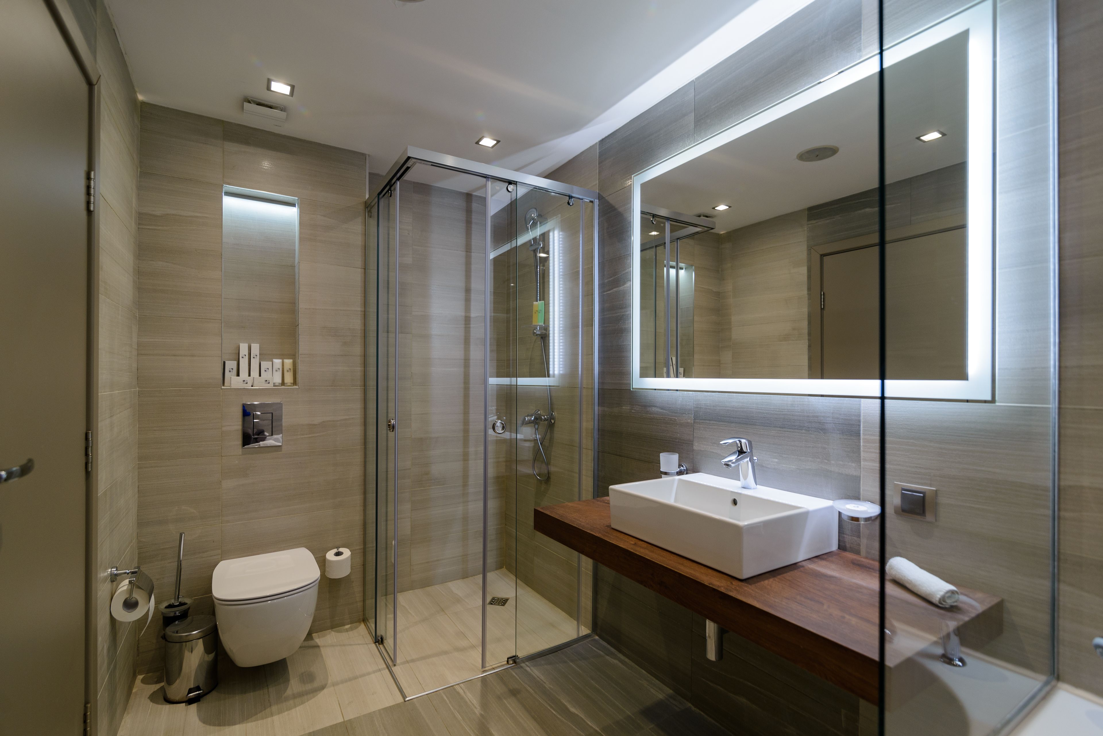 Un baño moderno con ducha de vidrio, un espejo grande y un mueble de tocador de madera.
