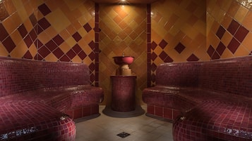 A spa room with two red cushioned seating areas, a central pillar, and a tiled wall with a diamond pattern.