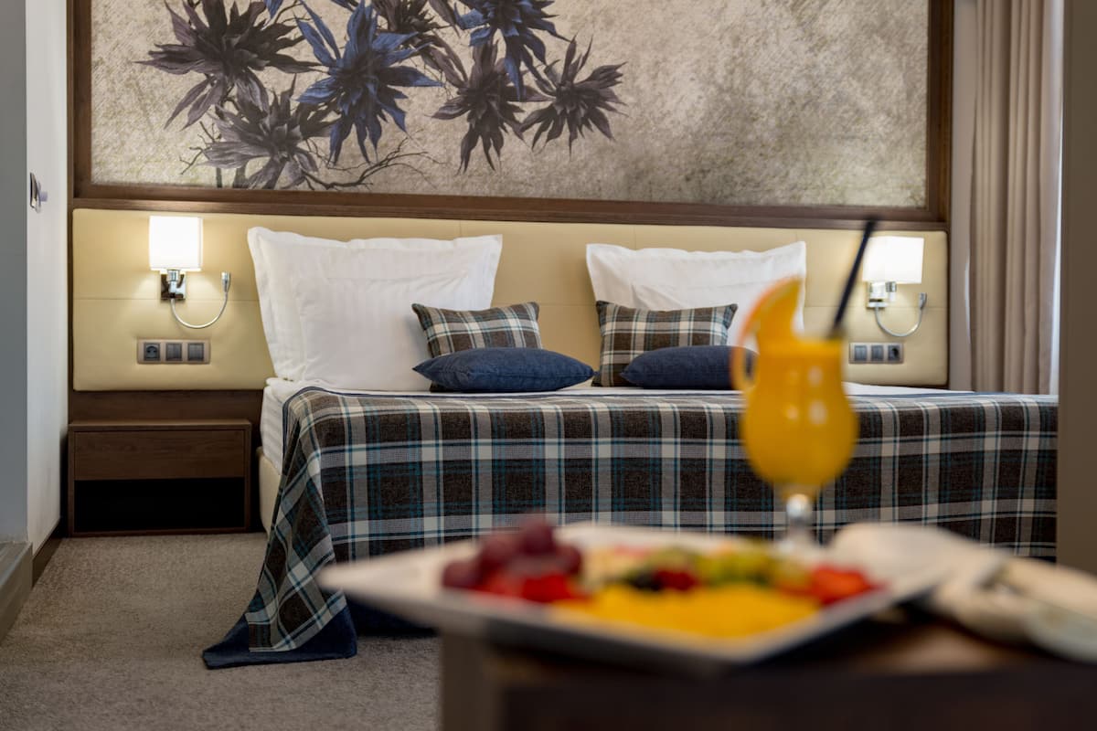A hotel room with a bed, two bedside tables, a nightstand, a wall-mounted lamp, and a fruit plate on the nightstand.