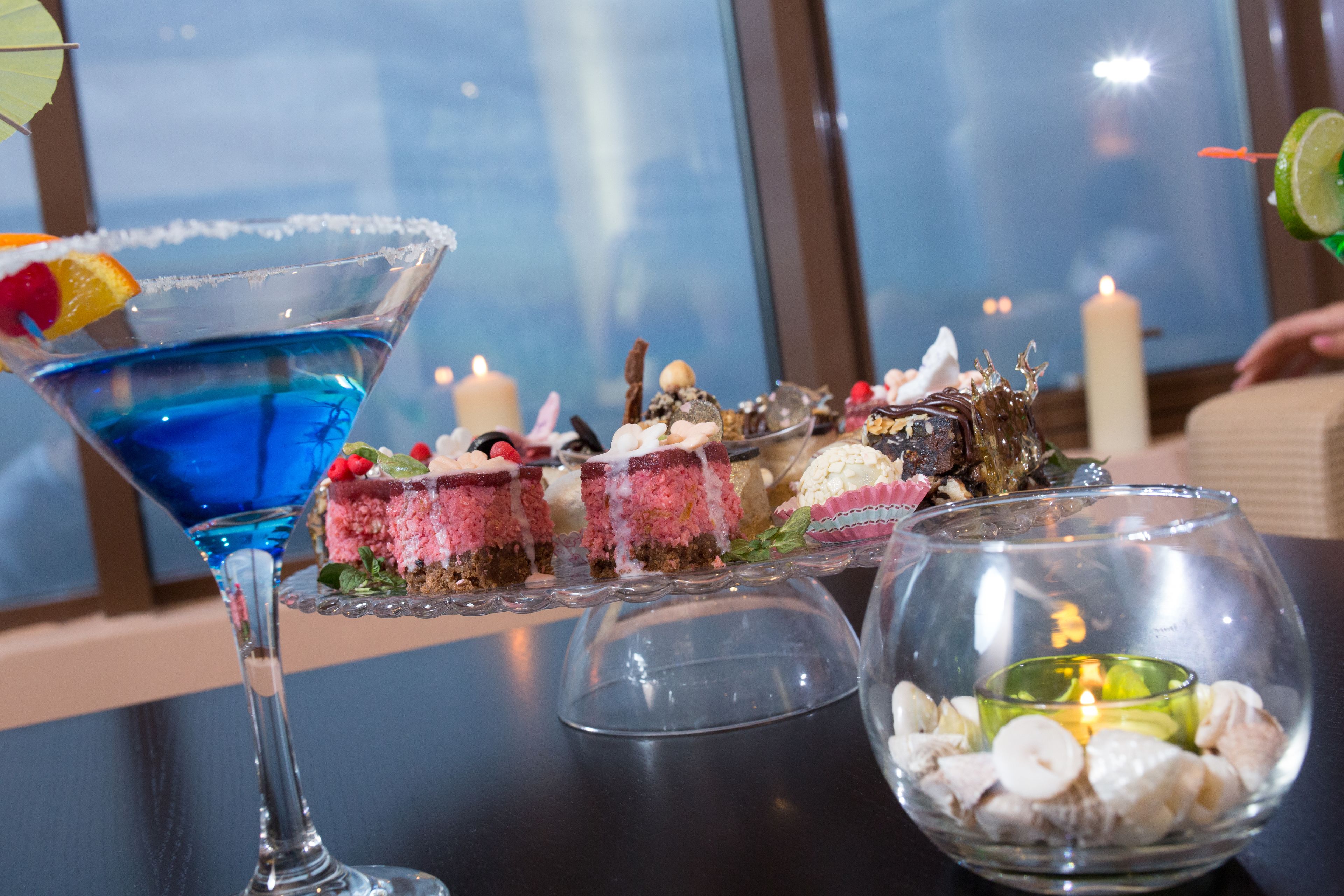 Una mesa de postres con un cóctel azul, varios pasteles y una vela.