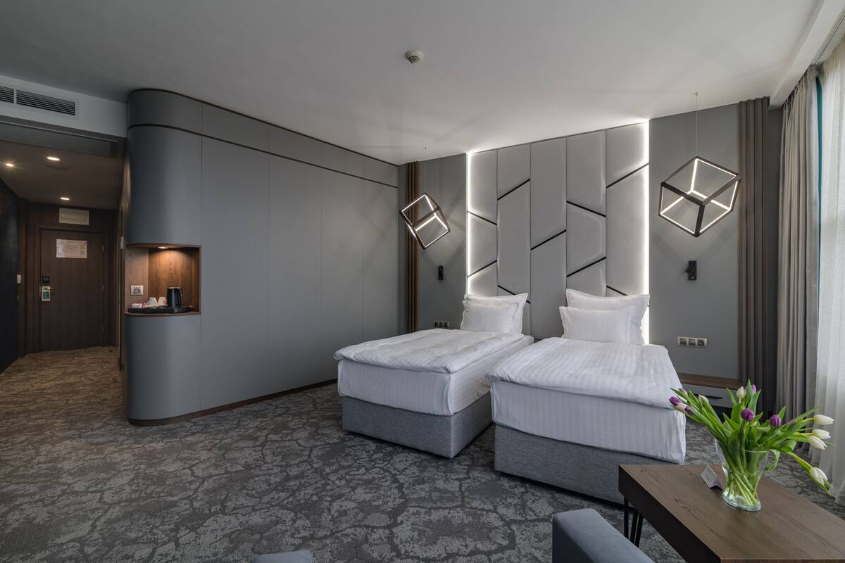 A modern hotel room with two beds, a small desk, and a vase of flowers.