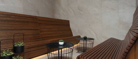 A modern interior with a wooden slatted wall, three black metal tables with potted plants, and a curved wooden bench.