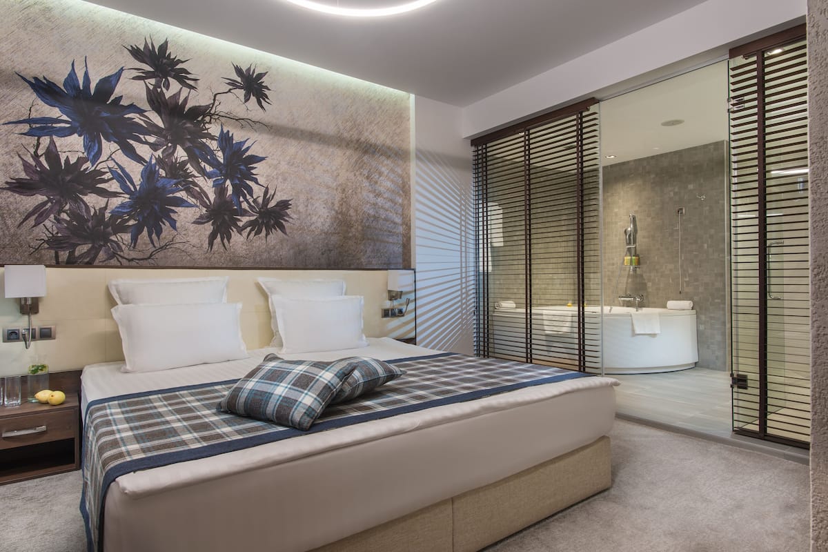 A modern bedroom with a large bed, a wall-mounted artwork, and a sliding glass door leading to a bathroom.