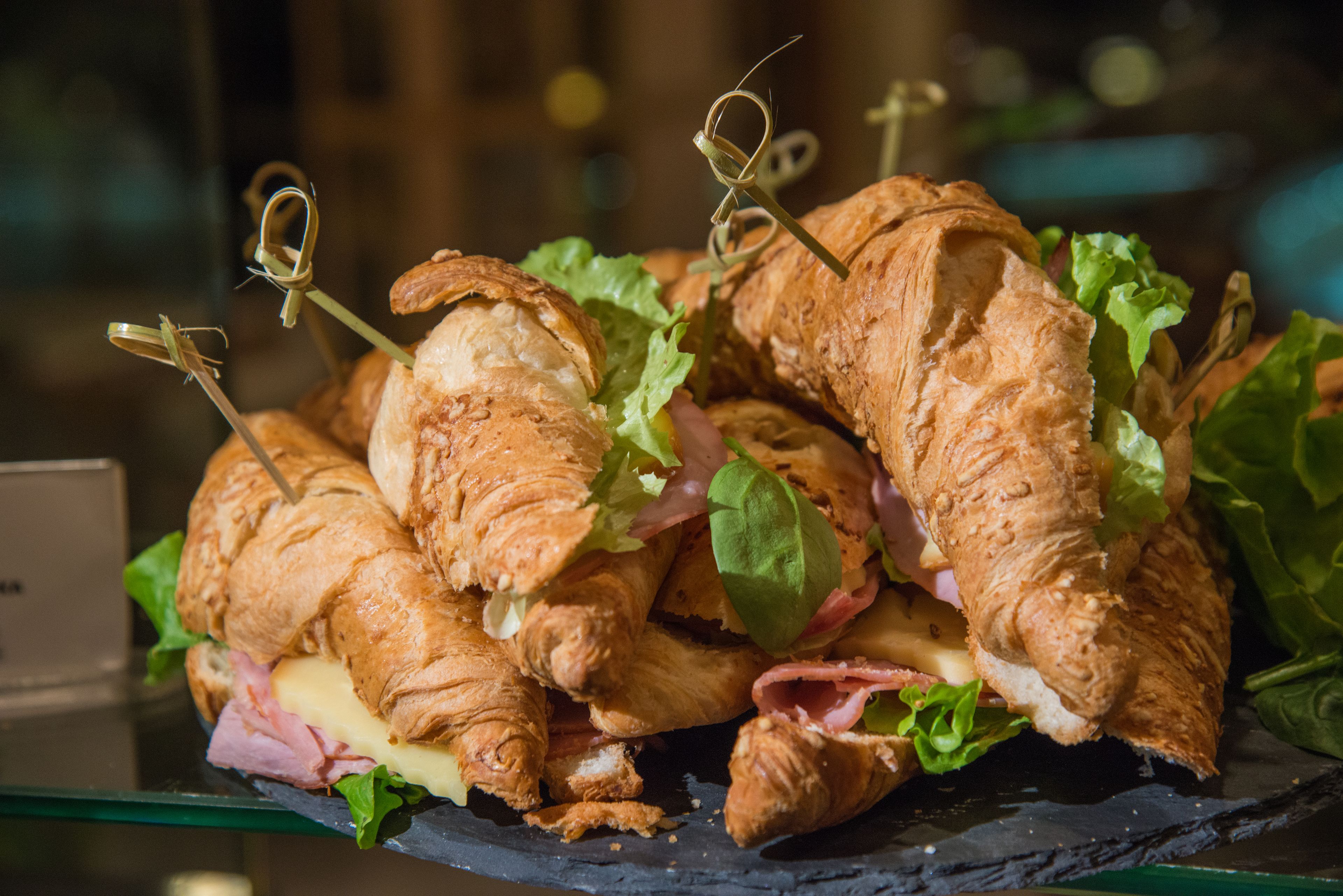 Presentación de sándwiches de croissant con palillos, rellenos de jamón, queso y lechuga.