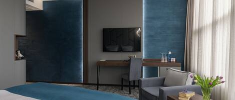 Una habitación de hotel moderna con una cama grande, un escritorio con una silla, un televisor de pantalla plana y una mesita con libros y un florero.