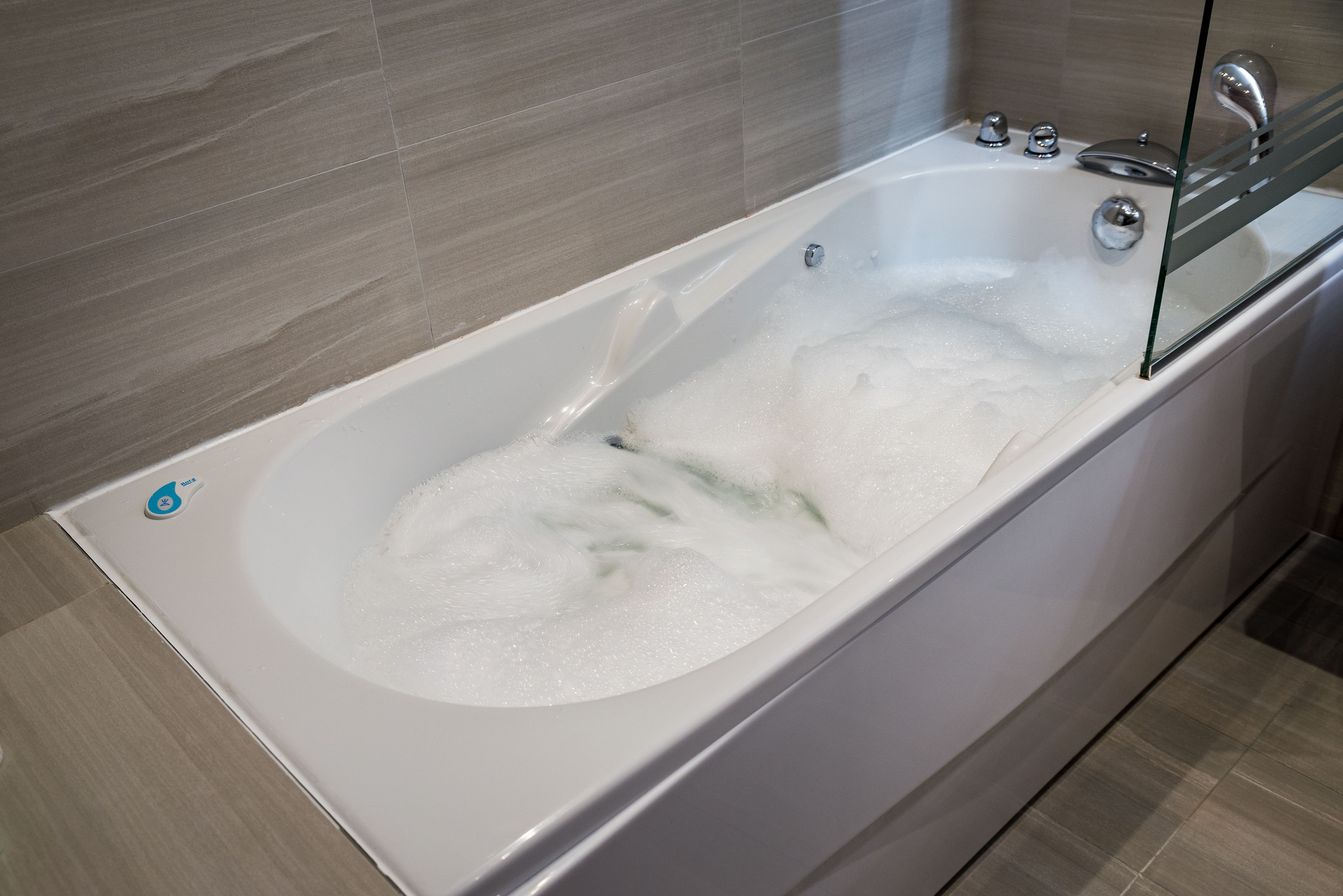 Een moderne badkamer met een bad vol bruisende bubbels, een douchecabine van glas en een betegelde muur.