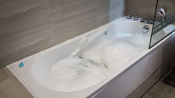 Een moderne badkamer met een bad vol bruisende bubbels, een douchecabine van glas en een betegelde muur.