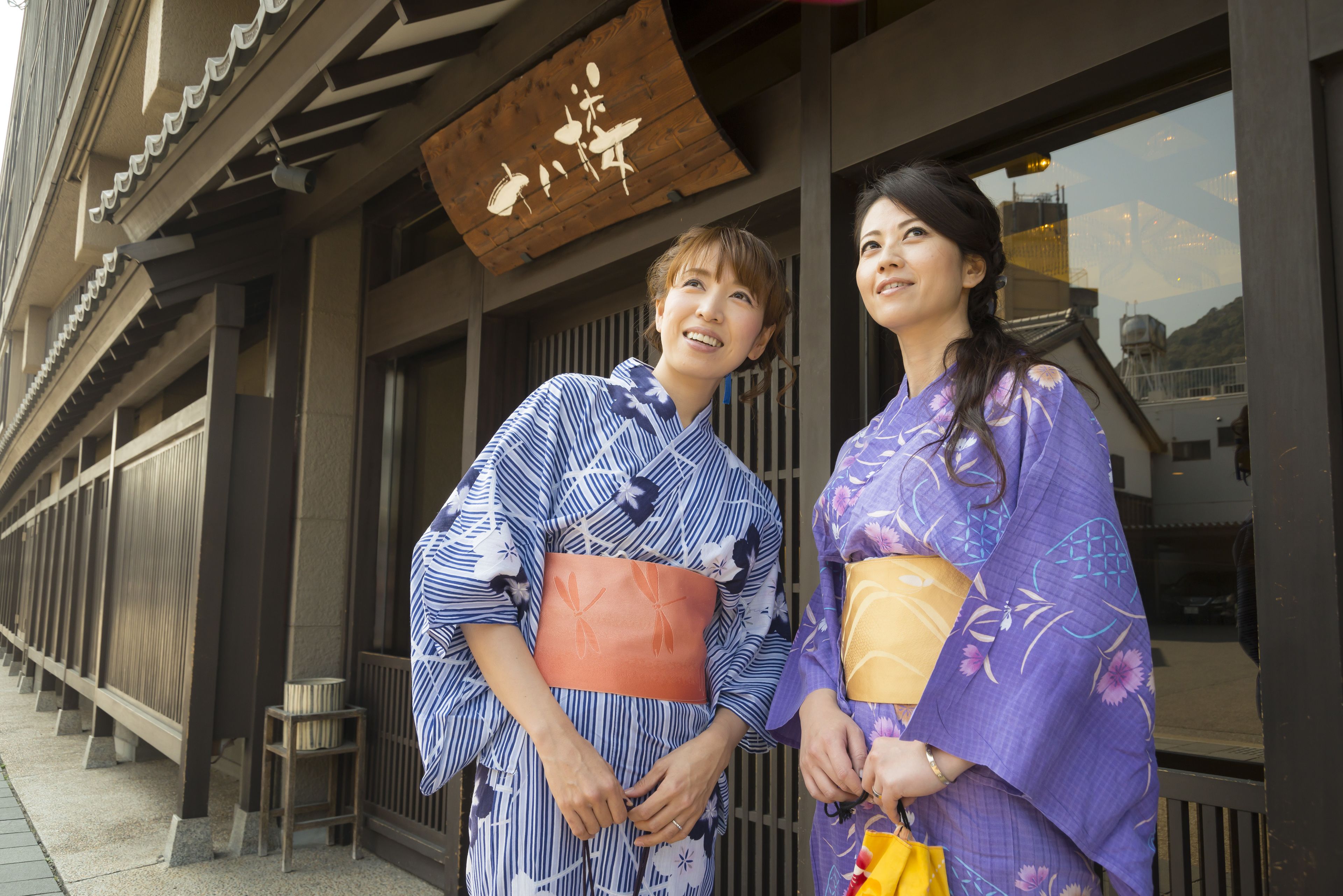 Two people in traditional Japanese attire standing in front of a building with a wooden sign.