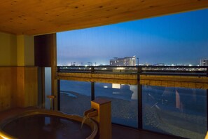 Uma área de spa com banheira de hidromassagem e uma grande janela com vista para a paisagem urbana ao entardecer.