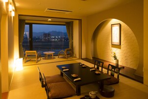 Habitación de hotel moderna con zona de comedor, ventanas amplias y vistas a la ciudad.
