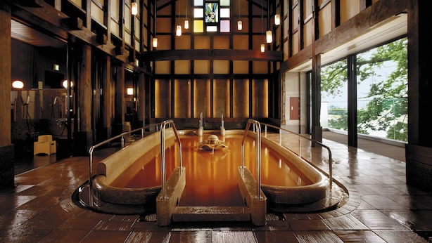 A traditional Japanese onsen with a wooden interior, a stone hot spring bath, and a view of trees through large windows. - Juhachiro (Gifu)