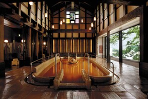 A traditional Japanese onsen with a wooden interior, a stone hot spring bath, and a view of trees through large windows. - Juhachiro (Gifu)