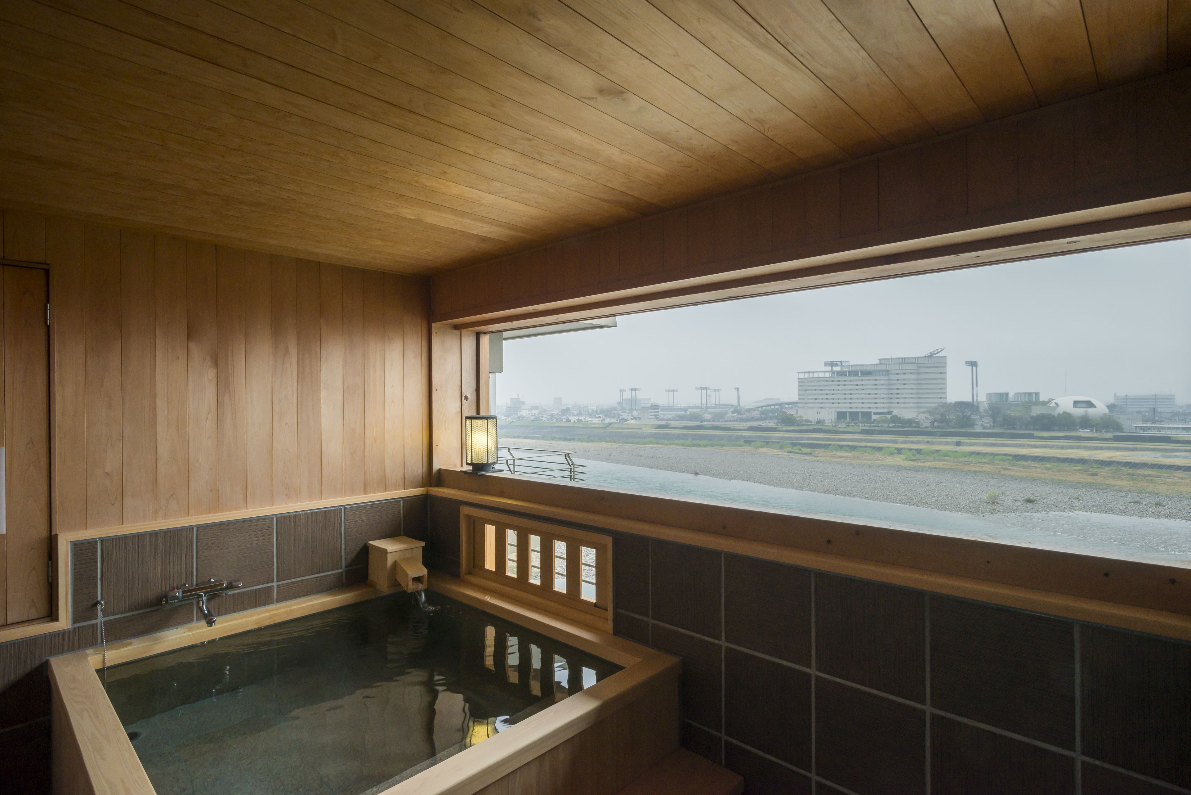 A wooden interior with a large bathtub and a view of a building across a body of water.