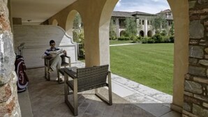 A covered outdoor area with a bench and a table, stone arches, and a view of a building with a lawn. - Garda Apartments San Vigilio Golf (Pozzolengo)