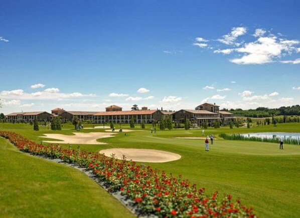 A golf course with a clubhouse, a pond, and a flower bed. - Garda Apartments San Vigilio Golf (Pozzolengo)