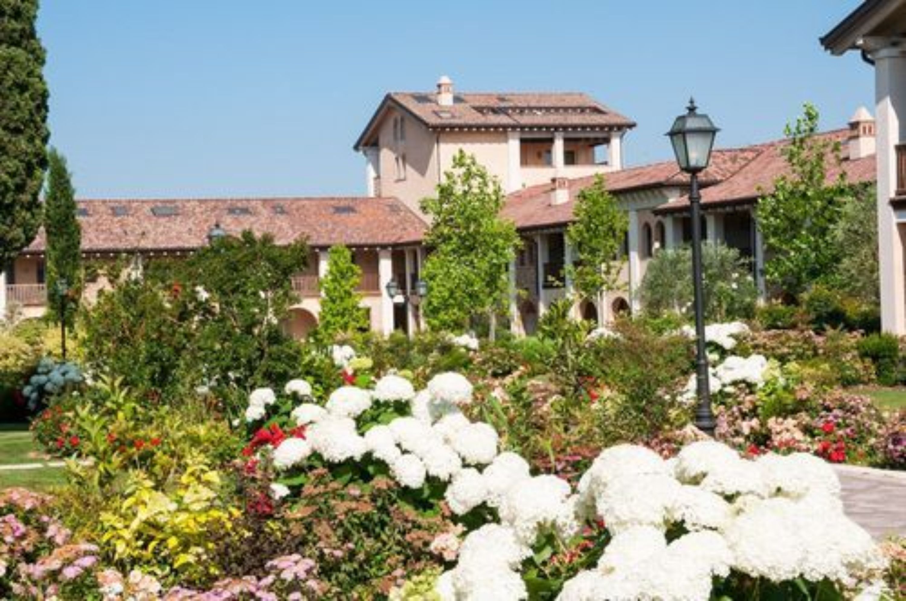 Un edificio con techo de tejas, ventanas arqueadas y un jardín con diversas flores.