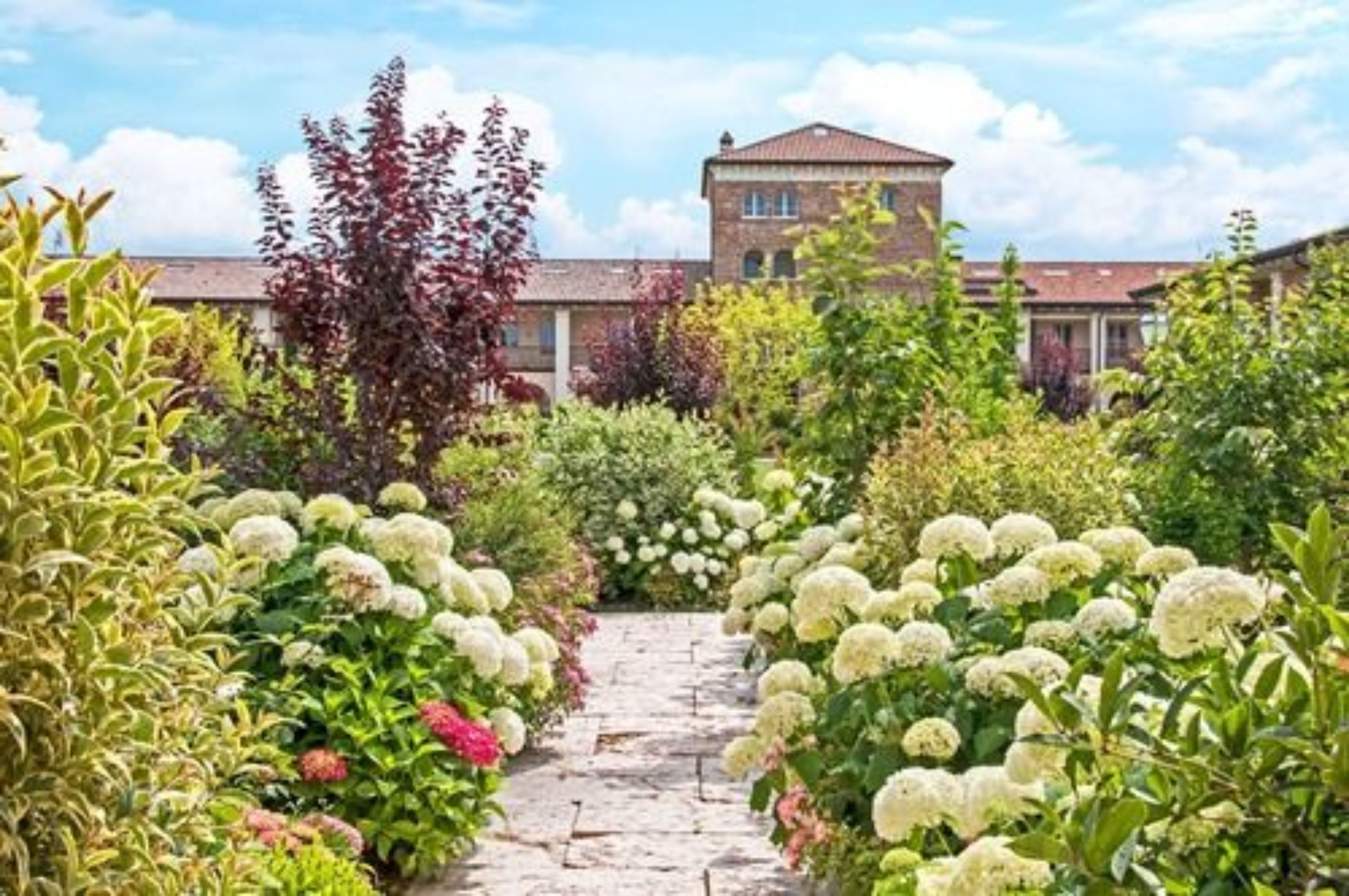 Un chemin de jardin qui mène à un bâtiment dont la façade est en briques et le toit est rouge.