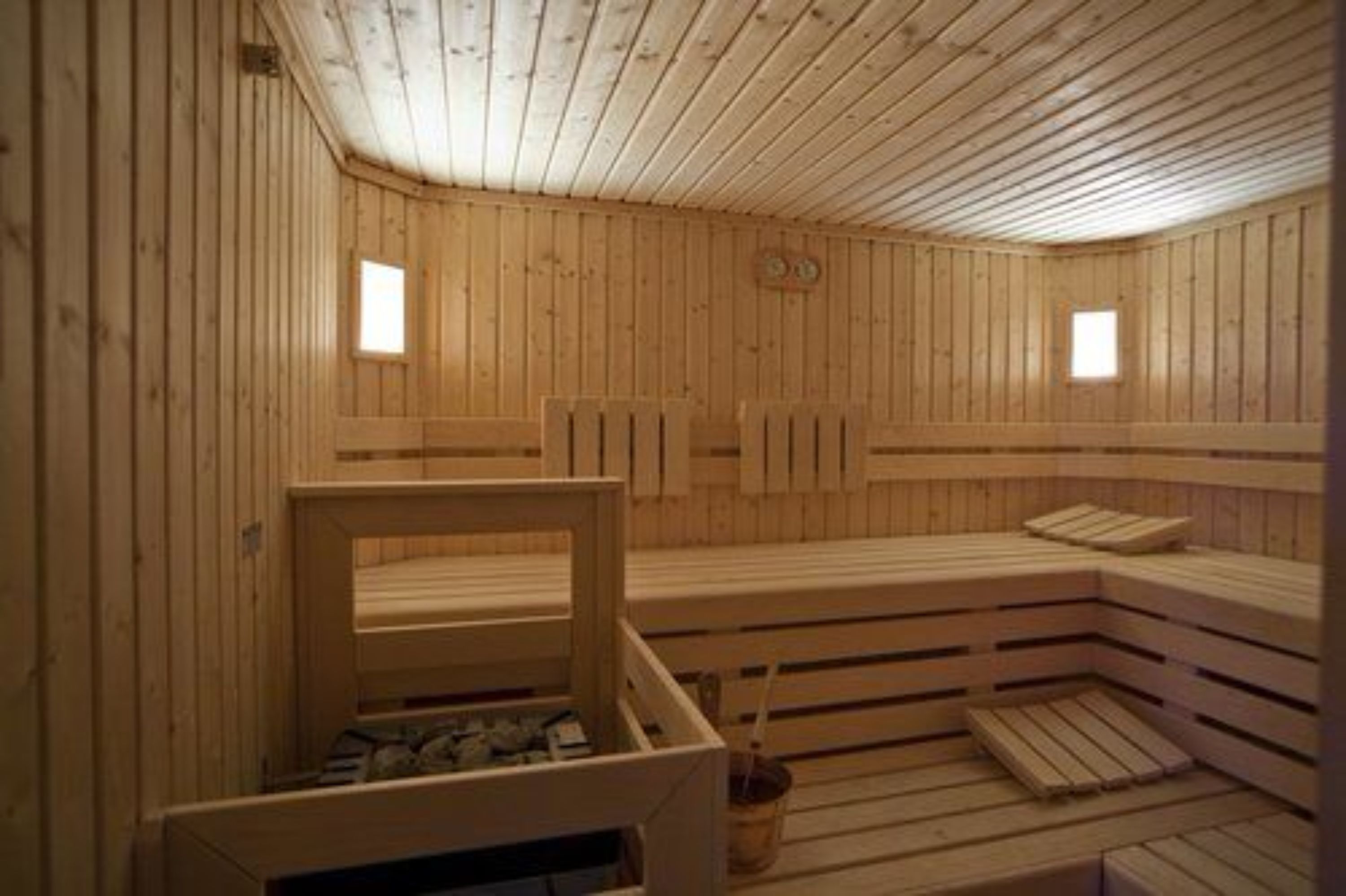 En träbeklädd bastu med sittbänkar och ett litet bord, träväggar och två fönster.