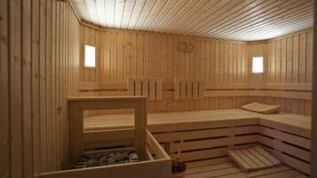 A wooden sauna with benches and a small table, wooden walls, and two windows.