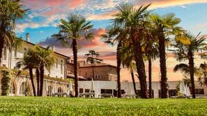 A building with a courtyard, palm trees, and a clear sky. - Garda Apartments San Vigilio Golf (Pozzolengo)