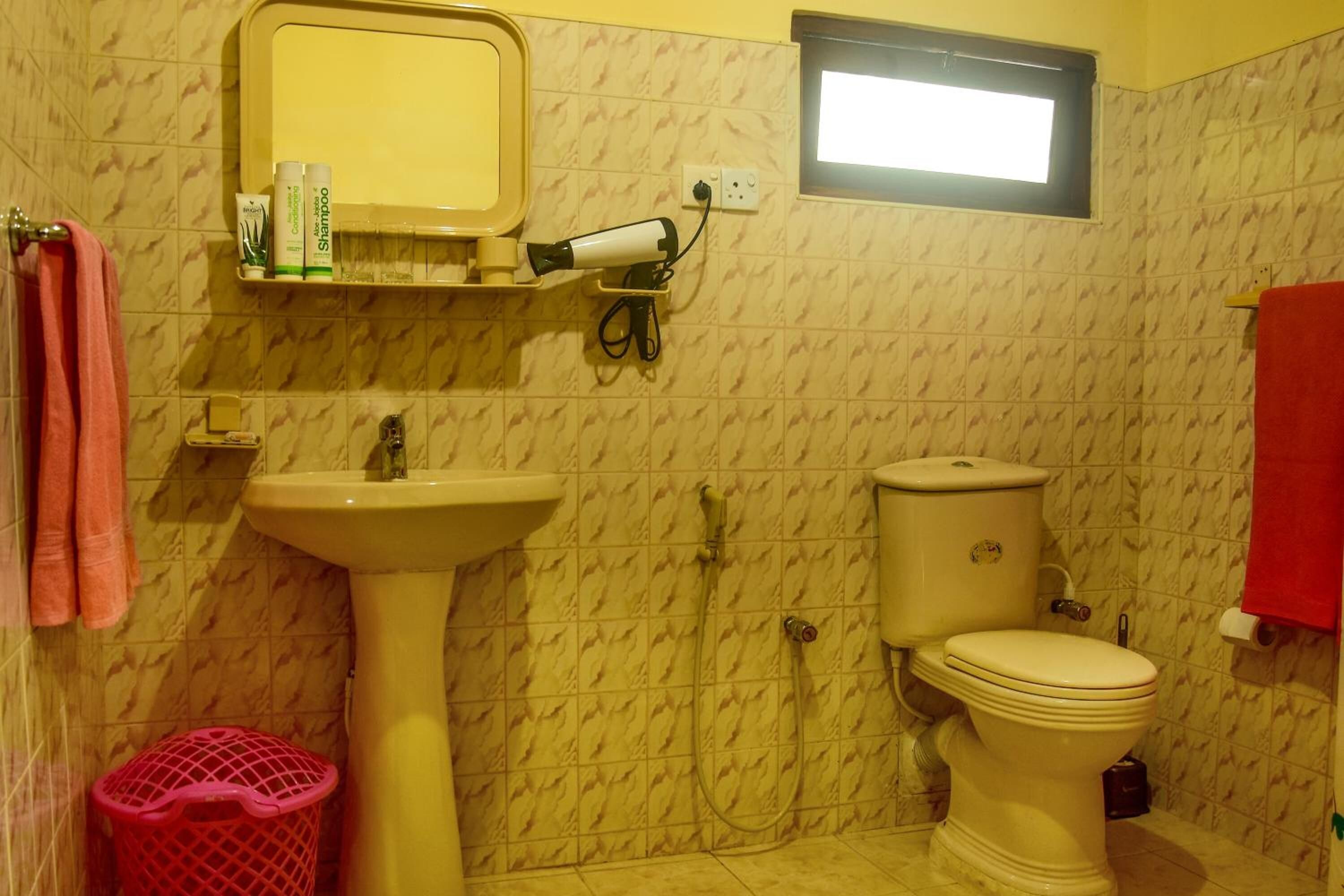 Une salle de bain avec un lavabo, des toilettes et une douche. Il y a un miroir au-dessus du lavabo et une fenêtre au-dessus des toilettes.
