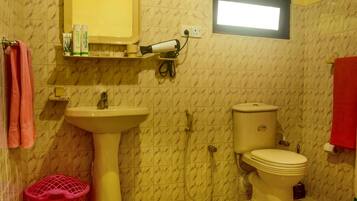 Une salle de bain avec un lavabo, des toilettes et une douche. Il y a un miroir au-dessus du lavabo et une fenêtre au-dessus des toilettes.