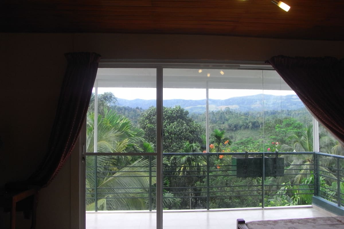 A room with a large sliding glass door leading to a balcony with a view of a lush landscape and mountains.