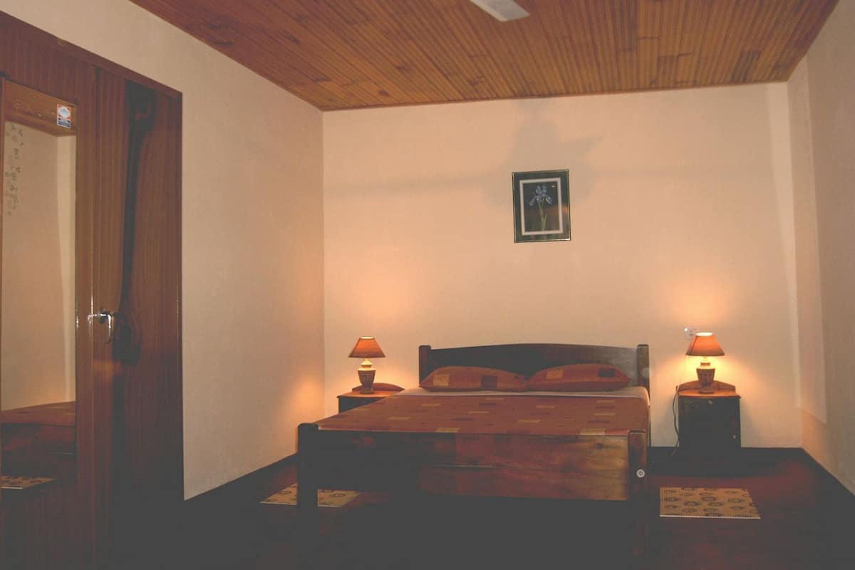 A bedroom with a wooden ceiling, a bed with pillows, two bedside lamps, and a framed picture on the wall.