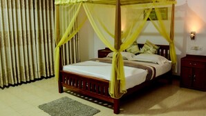 A four-poster bed with a canopy, a wooden nightstand, a small cabinet, and a wall-mounted light fixture. - Rainforest Lodge (Deniyaya)
