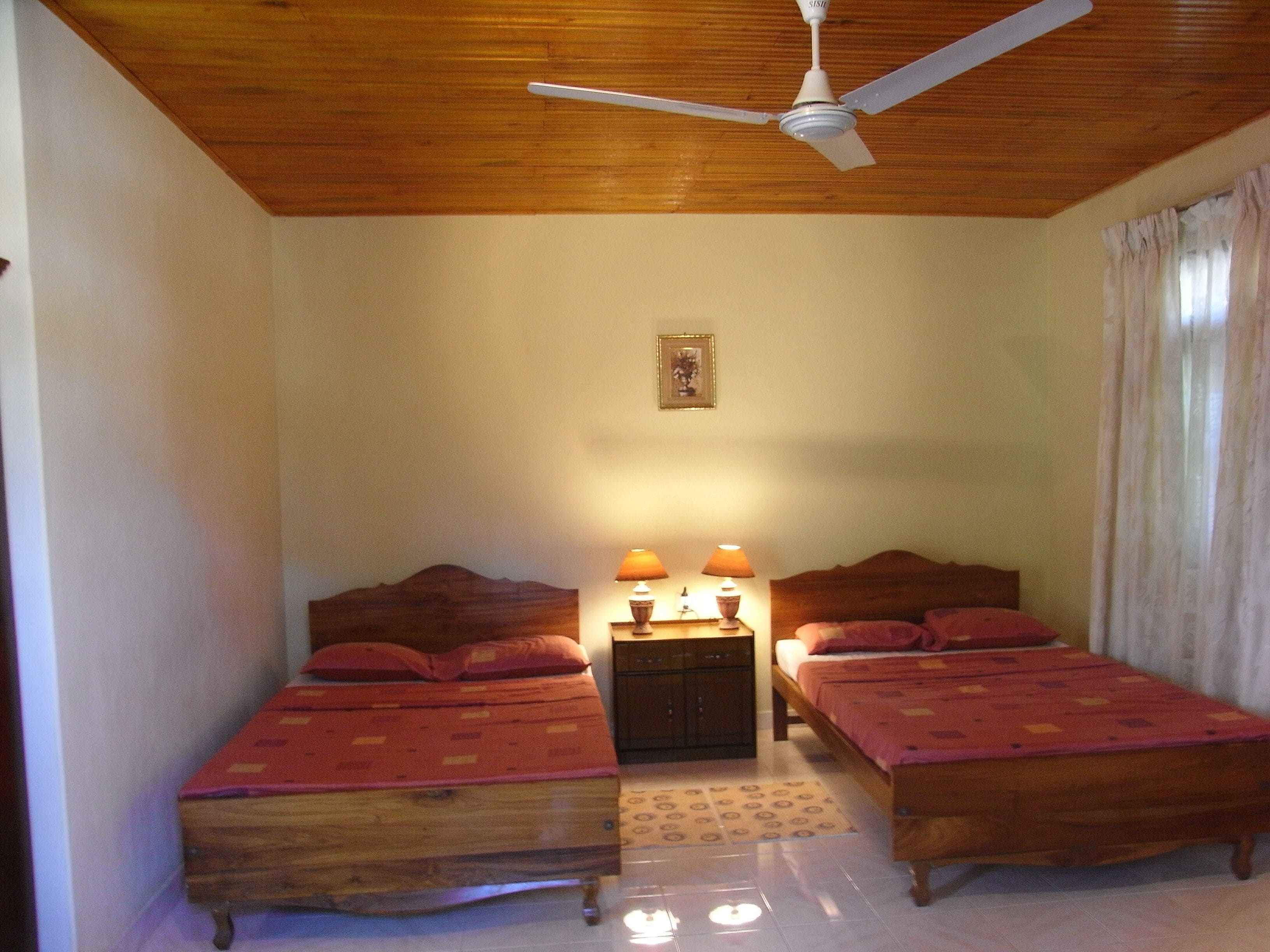 A bedroom with two wooden beds, a ceiling fan, and a nightstand with lamps.