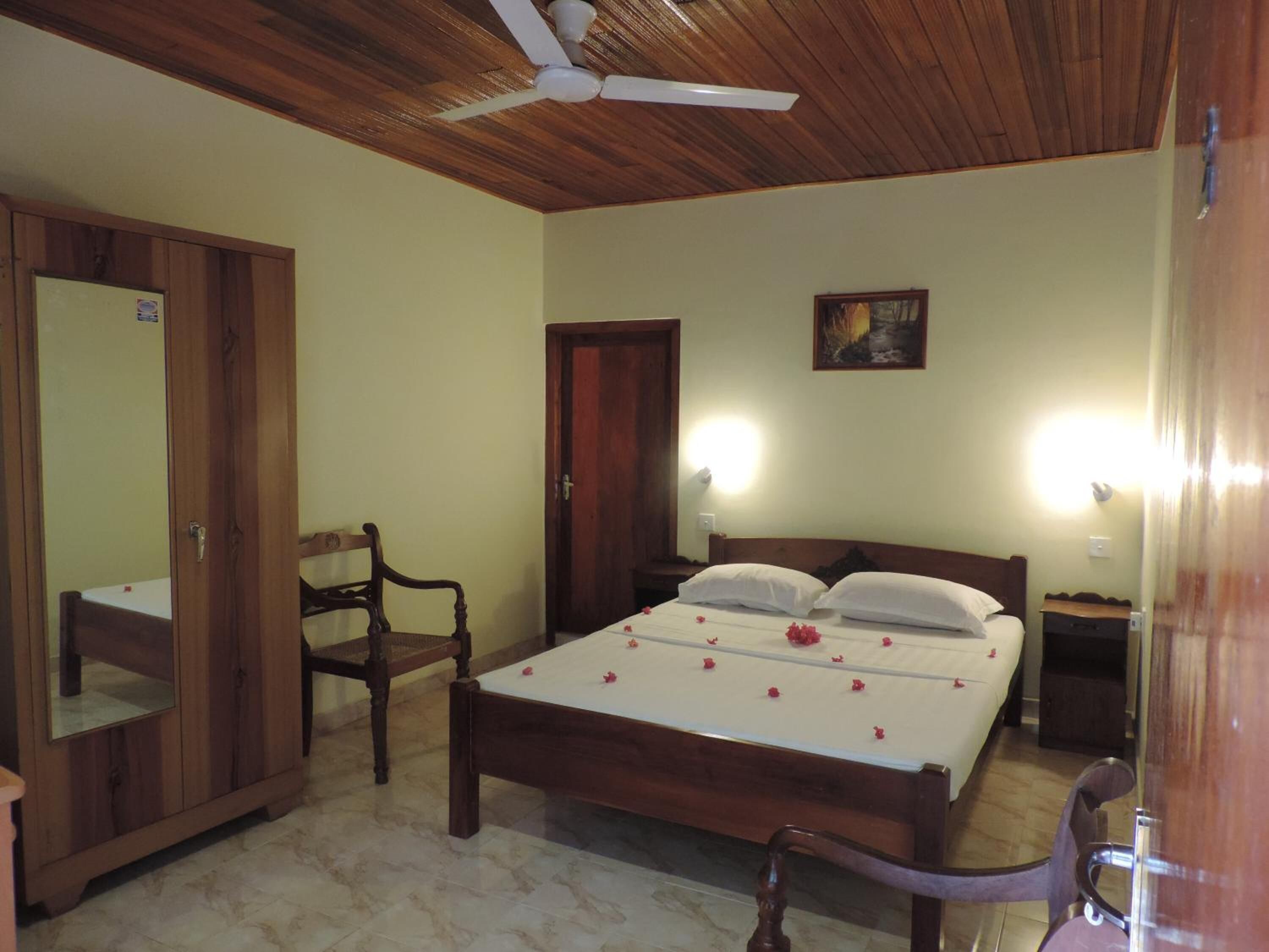 Un dormitorio con cama de madera, una silla, un armario, un ventilador de techo y un cuadro en la pared.