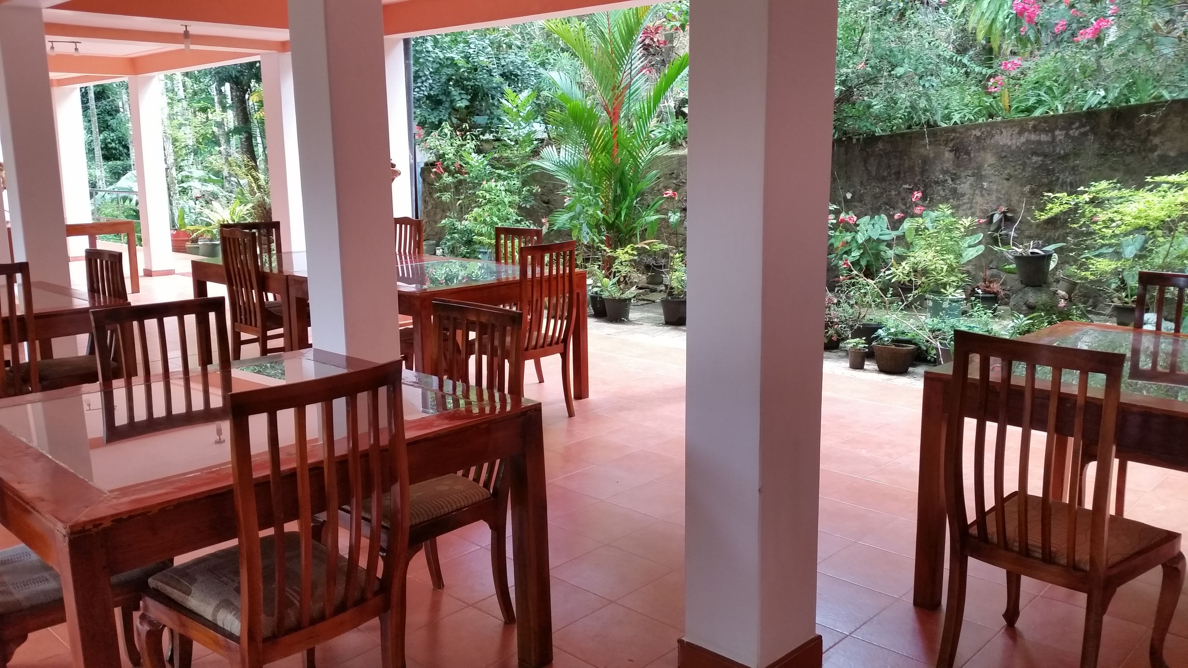 A restaurant with wooden tables and chairs, surrounded by potted plants and a garden view.