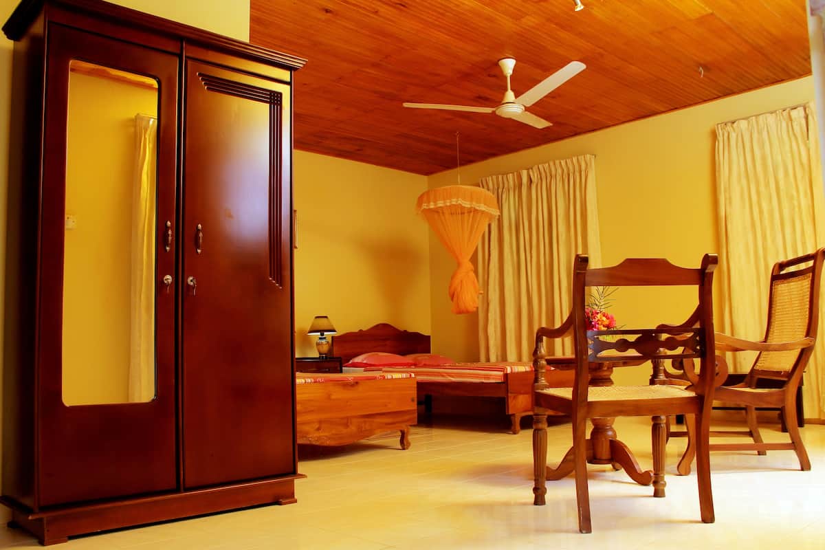 A bedroom with a wooden wardrobe, a bed with a canopy, a dining table with chairs, and a ceiling fan.