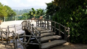 A rustic wooden bridge over a small water body, surrounded by lush greenery and a distant mountain range. - Rainforest Lodge (Deniyaya)